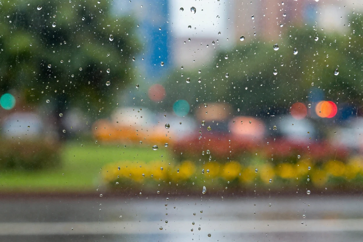 Close-up of a raindrop-covered window with a blurred colorful backdrop.